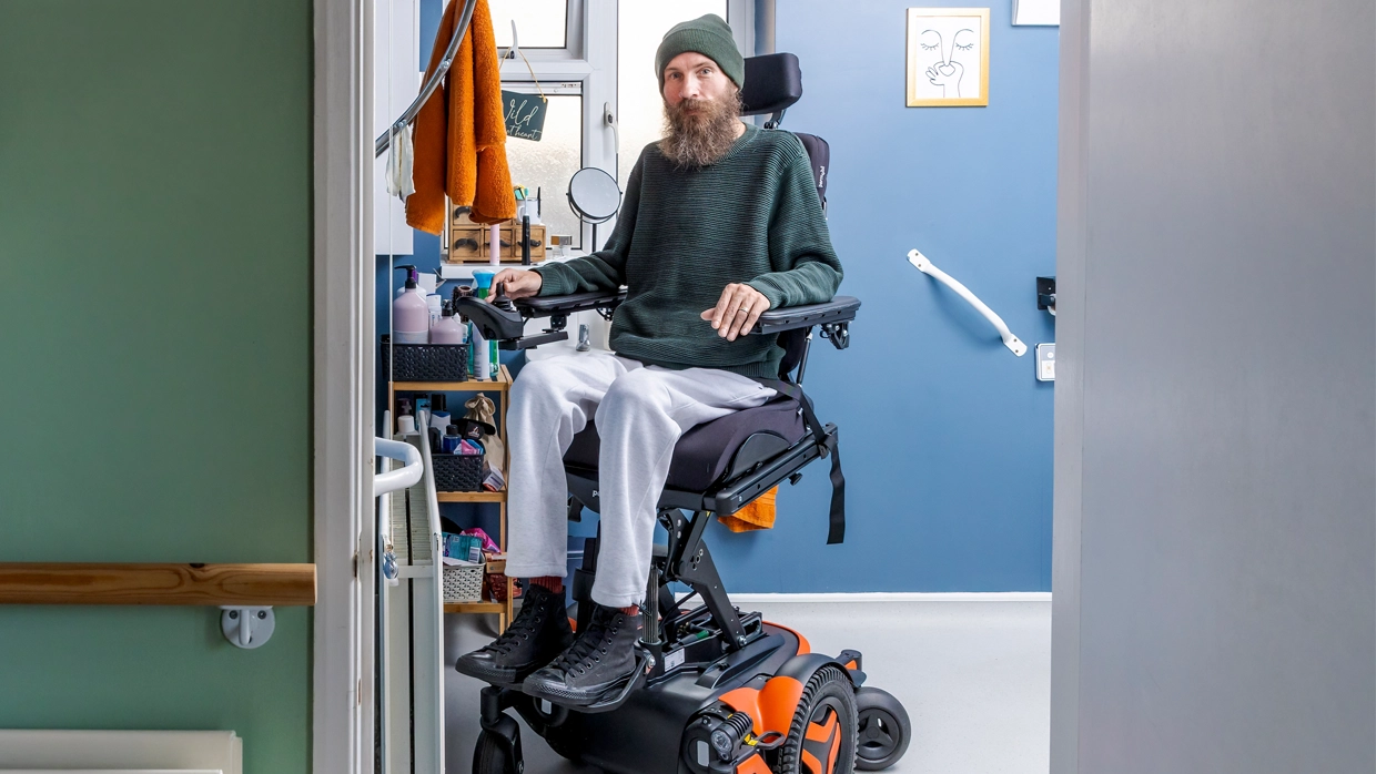 an-adult-mail-wheelchair-user-sitting-in-an-elevated-wheelchair-in-his-wet-room.webp