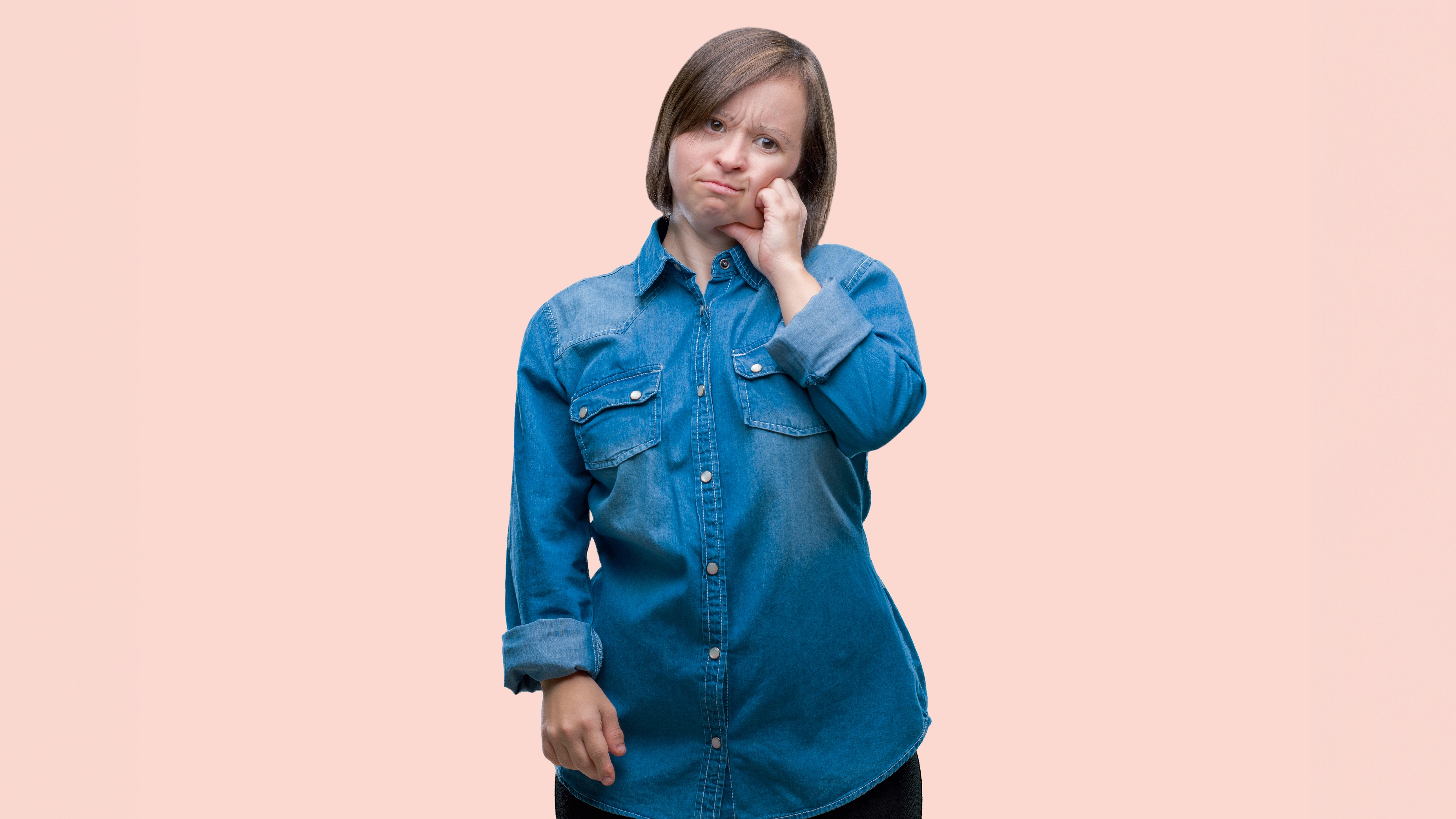 A person on a pink background holding their cheek in discomfort
