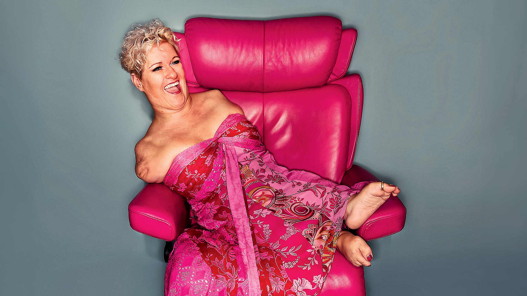 Photo of Alison Lapper wearing a pink dress and sat on a pink chair 