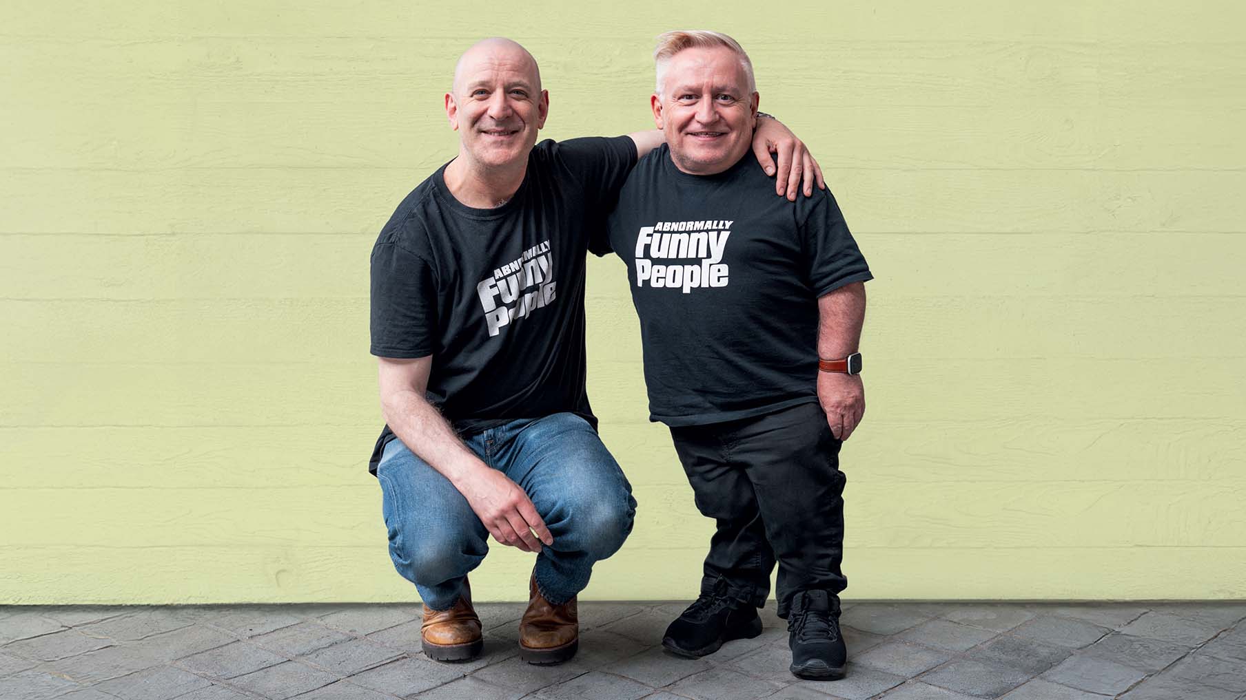 Simon Minty (right) and Steve Best (left) from Abnormally Funny People pose in front of a neutrally coloured wall backdrop
