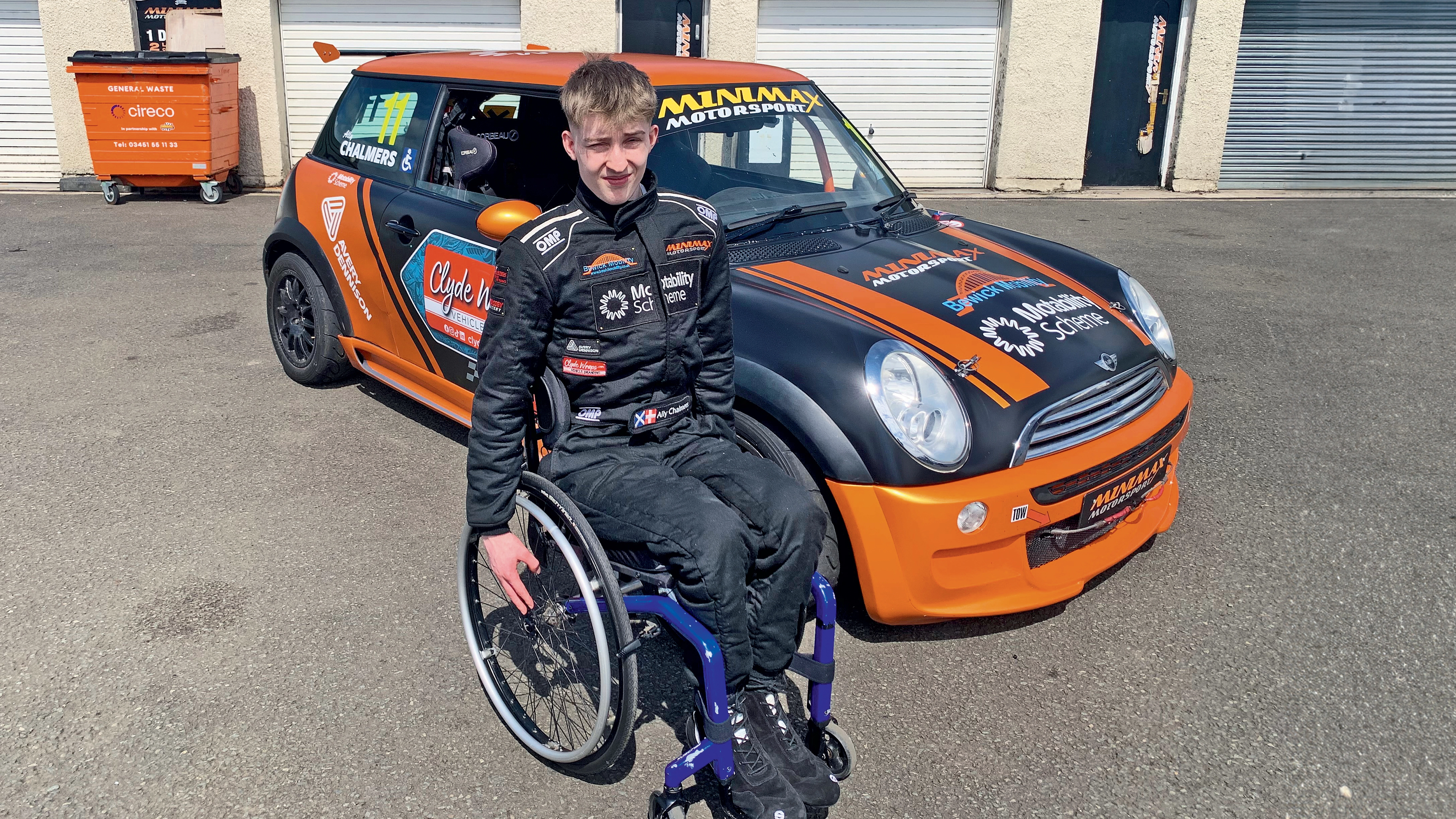A photo of the young race driver in a wheelchair in front of his car