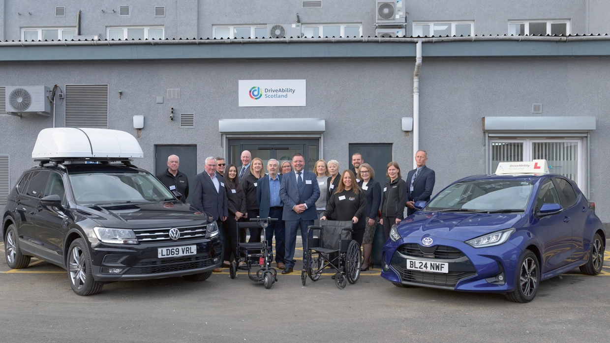 The staff of DriveAbility Scotland stood outside their HQ, flanked by a small SUV and small hatchback