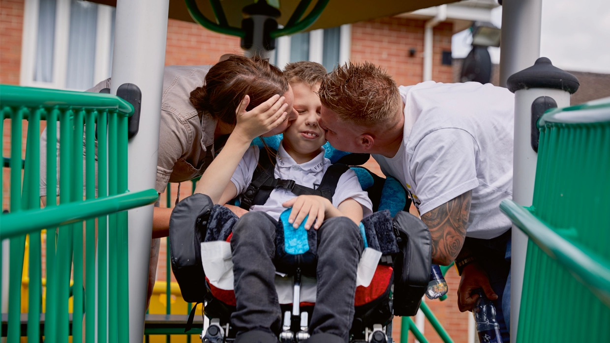 A young male wheelchair user (child) being embraced by his mother and father