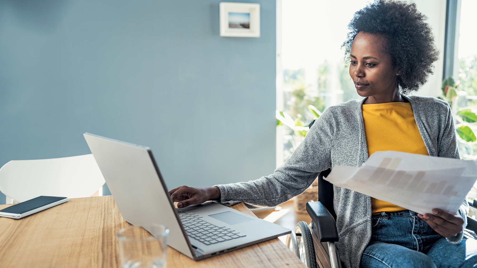 Women in a wheelchair holding a paper and looking at her laptop 