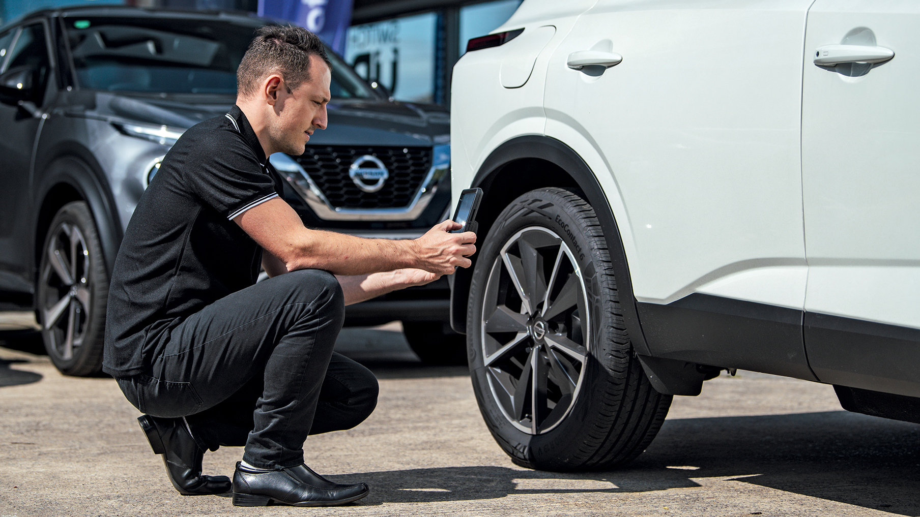 Man working on a tyre of a car. He is wearing all black and the vehicle is white