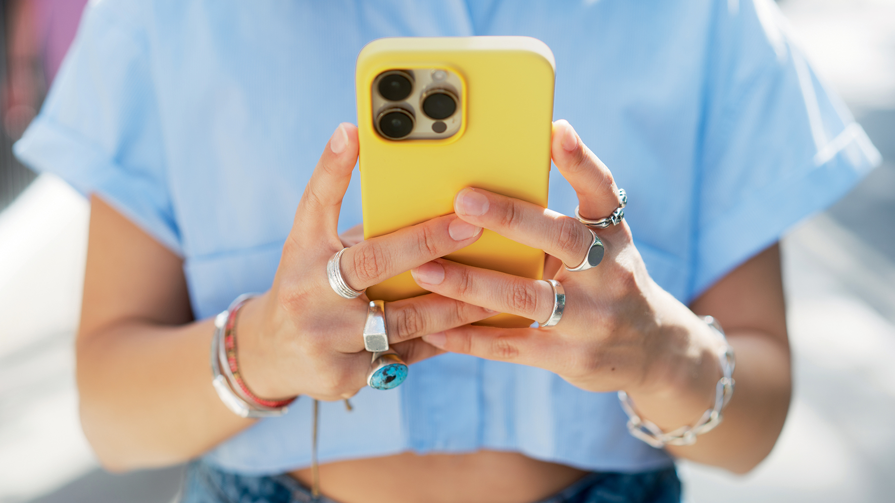 A women wearing a blue shirt and holding a phone with a yellow case