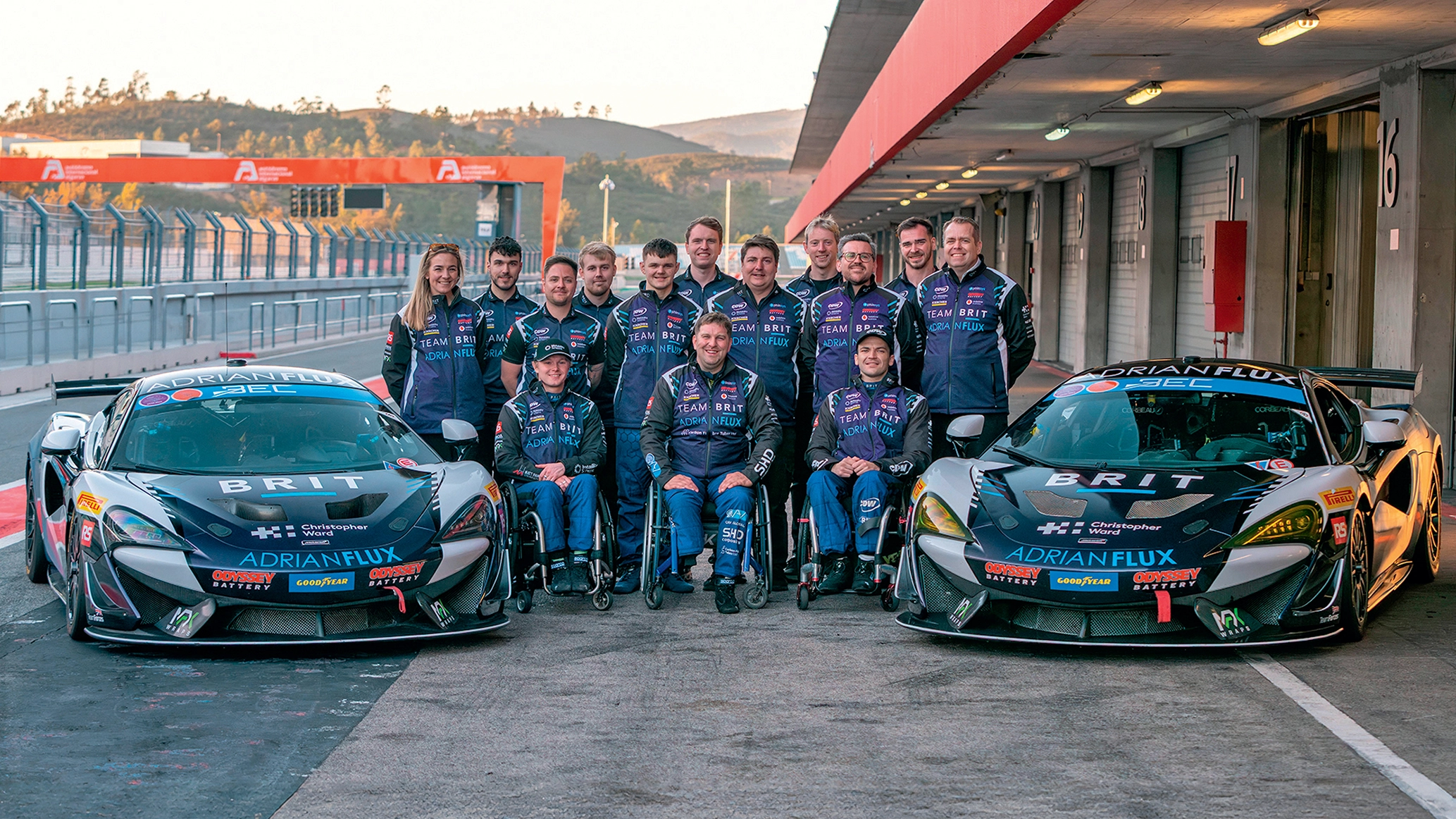 Team Brit posing between two race cars in pit-lane