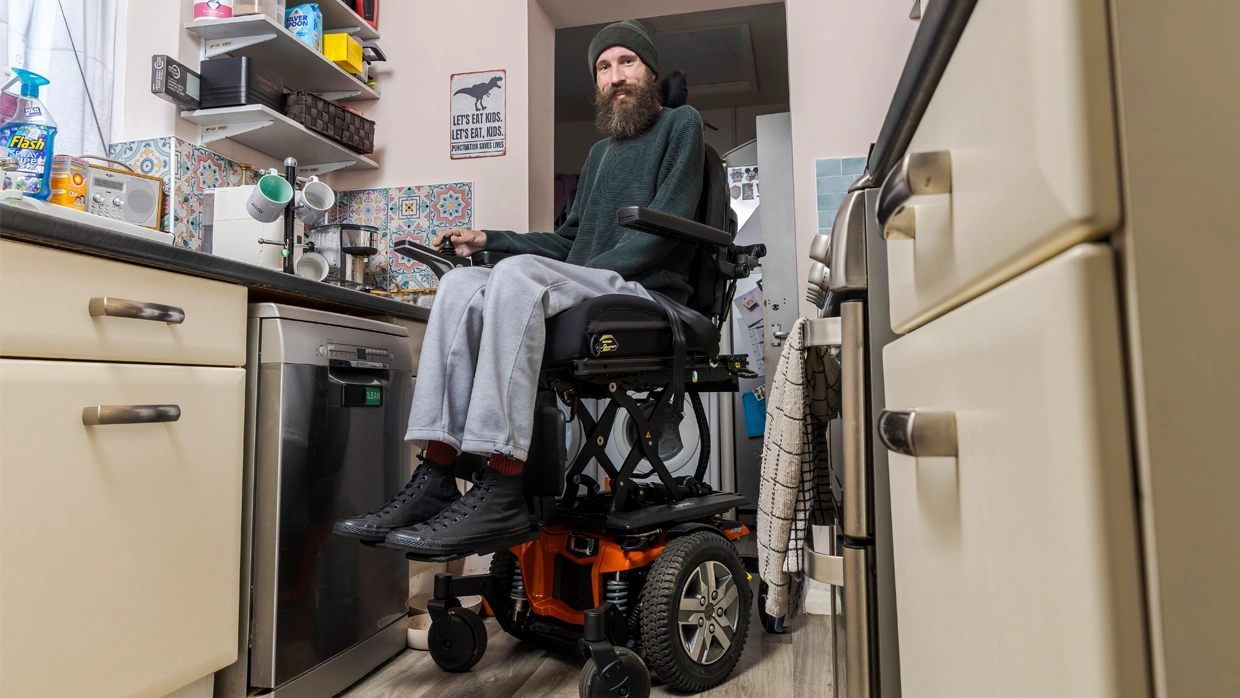 An adult mail wheelchair user sitting in an elevated wheelchair in his kitchen