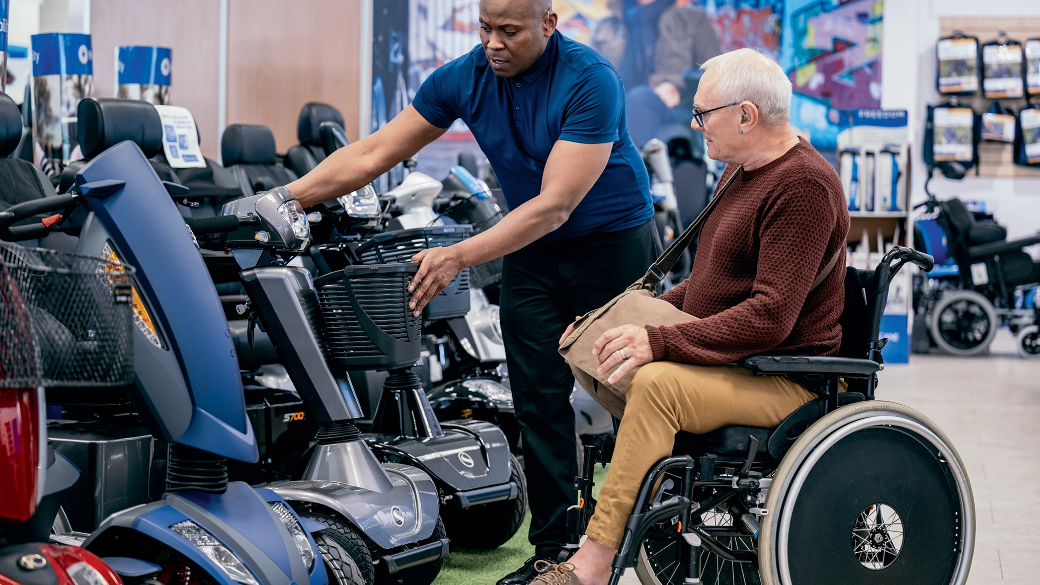 A staff member showing a wheelchair user a stock of mobility scooters