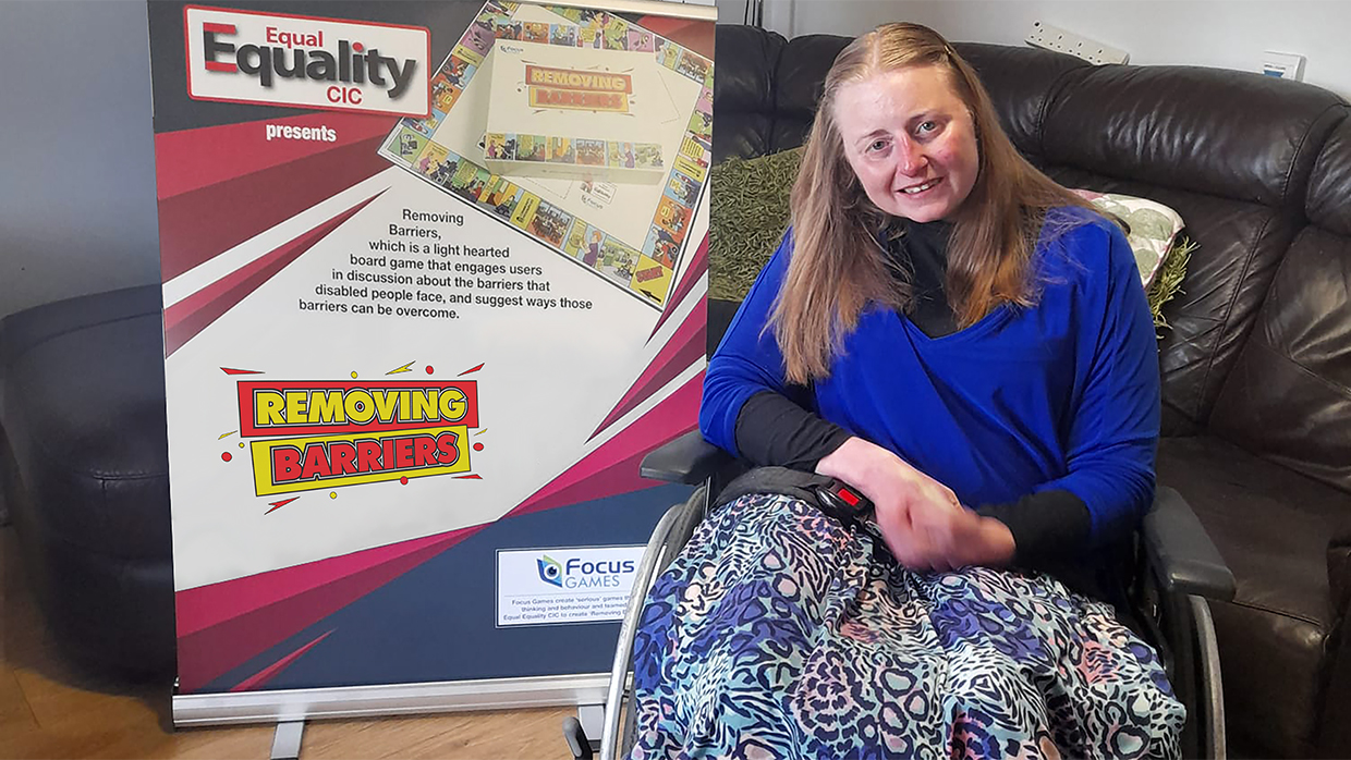 Toyah sitting next to a banner with her board game on it 